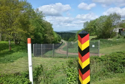 Im Vordergrund ist eine schwarz-rot-gelbe Grenzsäule zu sehen, dahinter der ehemalige Grenzzaun an der innerdeutschen Grenze.